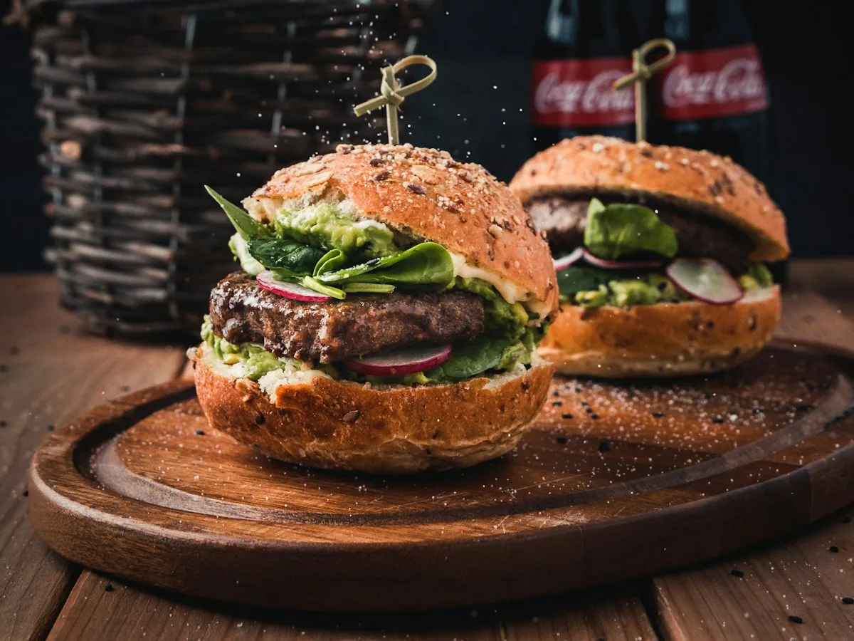 Dwa burgery na drewnianej desce z napojami w tle