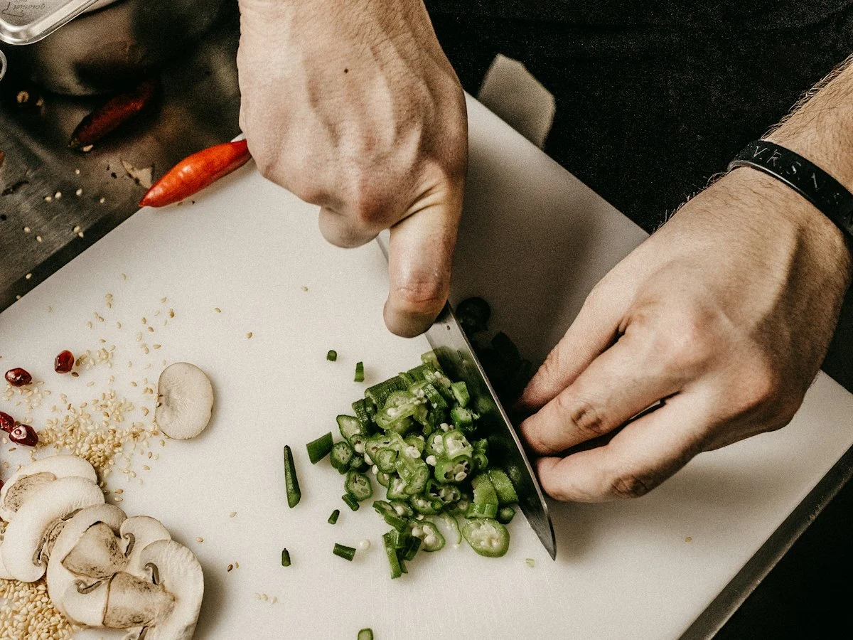 A cook chopping spring onions and vegetables on a board